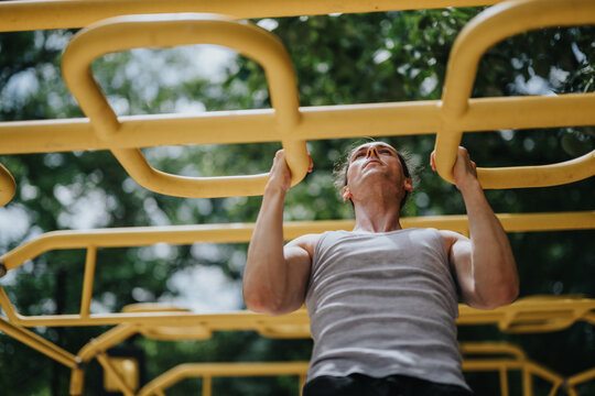 Young man performing pull-ups on yellow monkey bars. Athletic man working out on outdoor fitness equipment in a park.
