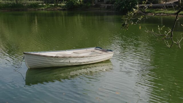 A small white rowboat floating calmly on a serene green pond or lake, surrounded by gentle water ripples and natural reflections, creating a peaceful atmosphere.