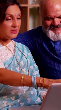 Asian Indian cute senior couple at their modern home enjoying leisure time together as they try to find information online, searching the internet  on a laptop