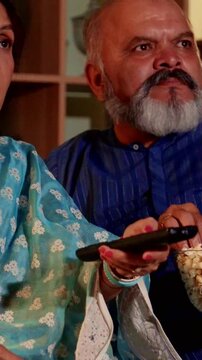 Retired Indian Couple Enjoying a Quiet Evening Watching a Horror Movie eating popcorn on a comfortable sofa at home 