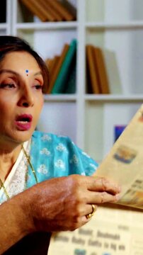 Indian retired senior couple enjoying a reading  newspaper together, sharing laughter and discussing daily news in their modern, cozy living room