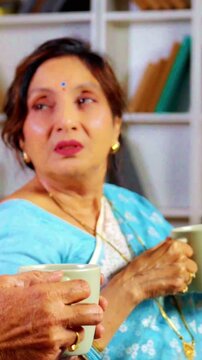 Beautiful Asian Indian retired couple enjoying a peaceful evening together, sipping tea and chatting in their modern drawing room