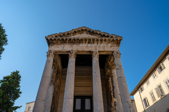 Pula, Croatia - August 22, 2025: Ancient Roman temple with tall Corinthian columns and weathered stone facade under clear blue sky.