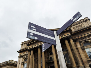 Obraz premium Historic directional signpost pointing to attractions in front of a classical museum facade in Liverpool, UK on an overcast day
