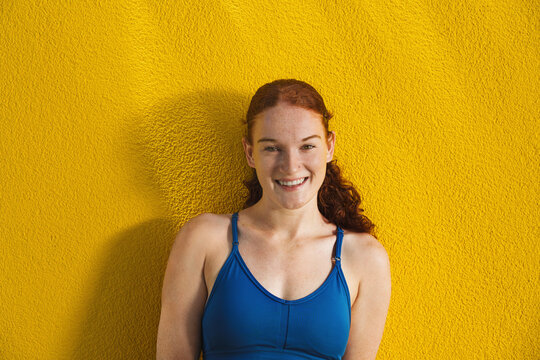  A young Caucasian woman with red hair and freckles smiles against a summer yellow background. Her expression is warm and inviting, showcasing natural beauty