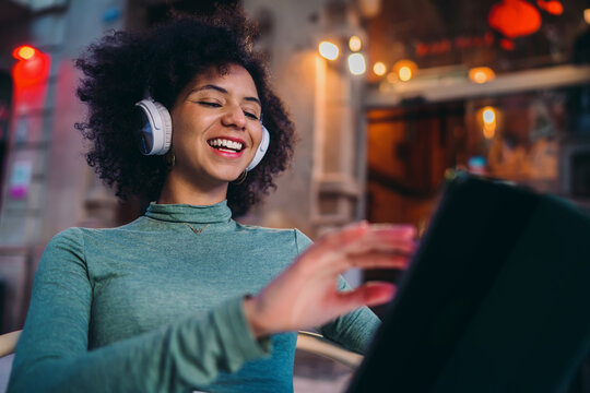 young woman laughing while enjoying a video conference chat application on mobile tablet display inside street cafe terrace, happy Gen Z girl talking online with remote friends desk