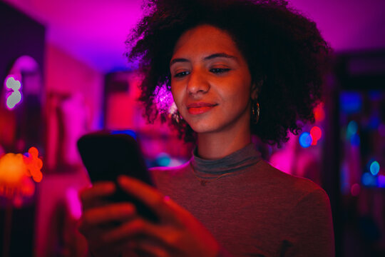 young tech savvy girl scrolling dynamic social media feed on modern smartphone screen under pink neon club lighting, focused Gen Z female user checking chat application notification