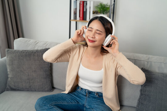 A young Asian woman wearing over ear headphones is happily enjoying listening to music.