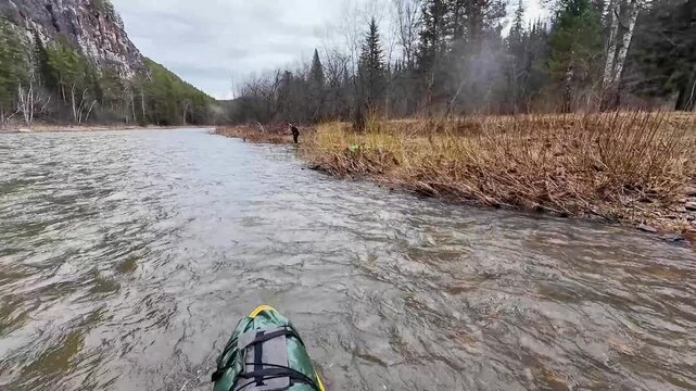 Assisting stranded kayak with paddle leverage. Rescue scene of kayak aid by paddler at riverbank. Practical river rescue involving kayak maneuver and paddle leverage at muddy shoreline