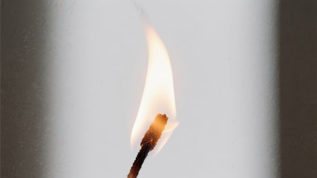 A close-up image of a burning matchstick with a bright flame against a plain background.