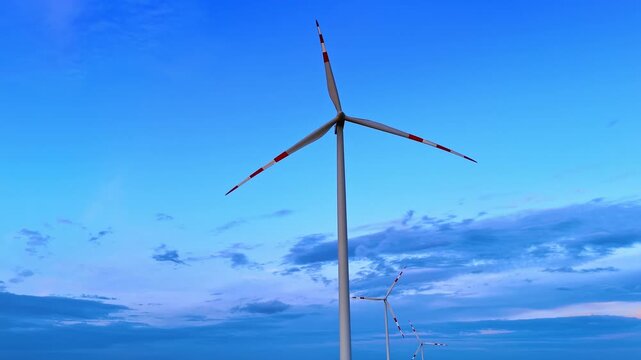 Large wind turbine against deep blue evening sky. Low angle view of steel propeller with red stripes on mast under cloudy twilight backdrop.