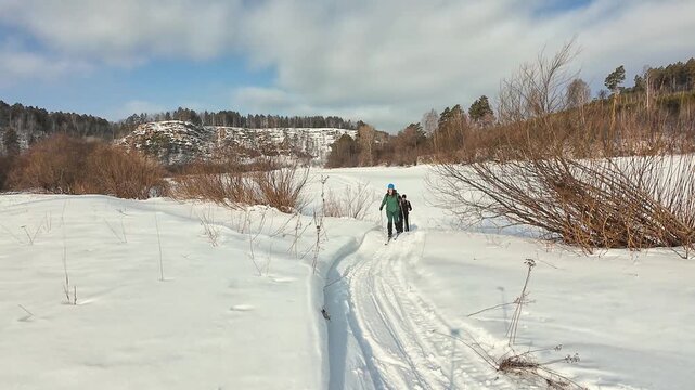 Snowy Trail Greeting. Sunlit Snow Path Where Skier Interacts Cheerfully With Companion. Bright Outdoor Scene Featuring Skier In Green Jacket Greeting Friend Along Snowcovered Trail