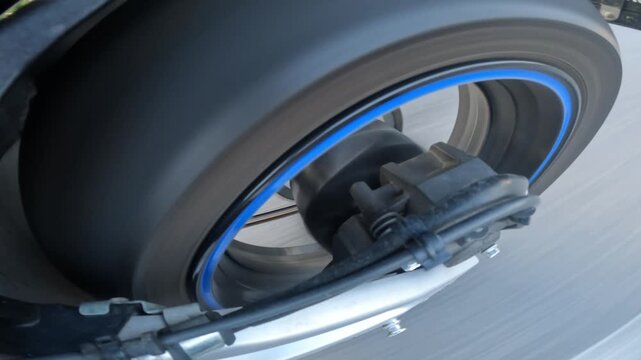 Low angle close view of wheel assembly with blue rim accent, black tire, central hub, axle housing, exposed bolts, and pedal hardware on paved road, with wheel, tire, rim, hub detail