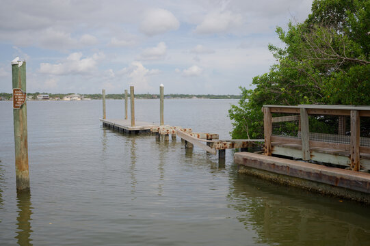 A weathered wooden boat ramp dock and narrow pier extend into calm bay water beside green mangroves. War Veterans Memorial Park In St. Petersburg, FL. Cloudy sky, evoking coastal tranquility, boating 