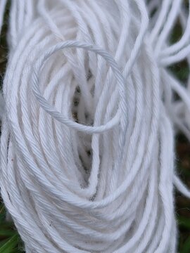 A tangled bundle of white cotton string or yarn resting on a patch of green grass in an outdoor setting during the daytime