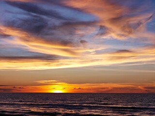 Obraz premium Vibrant sunset sky with dramatic clouds over a tranquil ocean horizon.