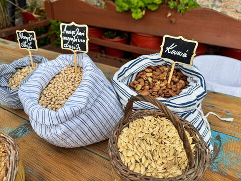 Traditional Greek legumes and grains in fabric sacks and wicker baskets with labels for manarolia peas, apostoliano white-eyed beans, fava broad beans and zea emmer wheat.