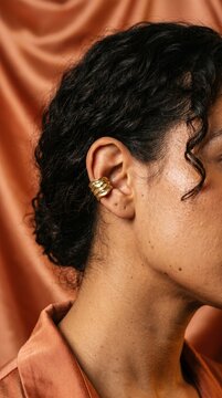 Latina woman ear with gold molten conch ear cuff on terracotta peach silk background