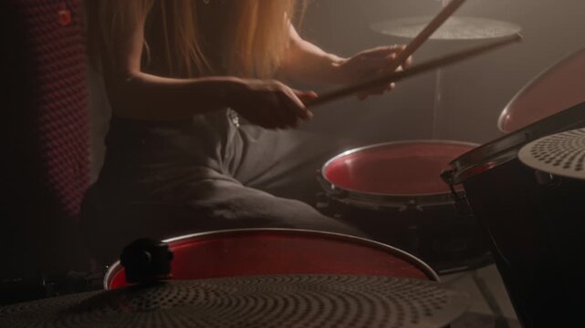 Tilt up rack focus shot of woman playing drums with drumsticks in music studio. Footage for music education marketing, instrument brand advertisements, or creative hobby campaigns