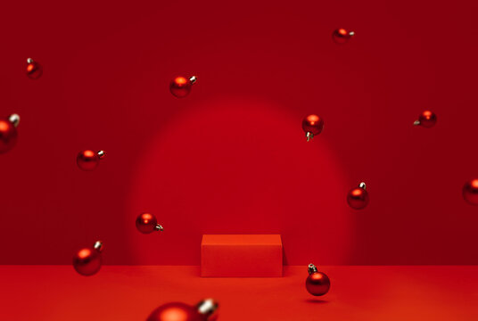 Dynamic red monochrome holiday studio scene with a rectangular product pedestal and multiple red Christmas ball ornaments floating and scattered throughout the frame under a glowing spotlight.