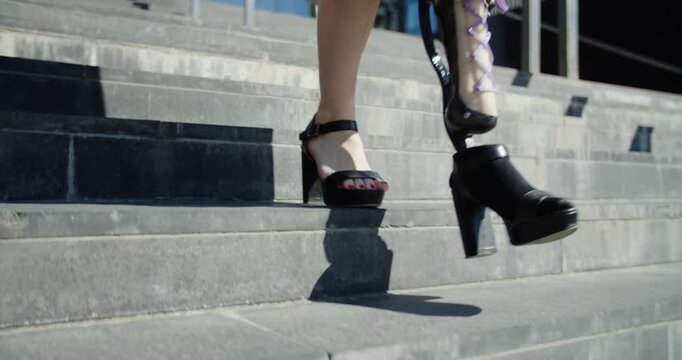 A person with a prosthetic leg walks confidently down stairs in high heels.
