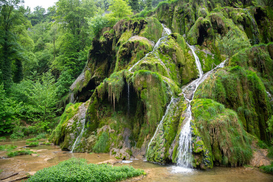 Moss-Covered Waterfall Cascades Through Lush Green Forest With Rocky Terraces And Tranquil Pool