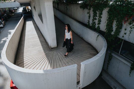 Senior business woman walks alone on a curved concrete ramp wearing professional clothing and sunglasses.