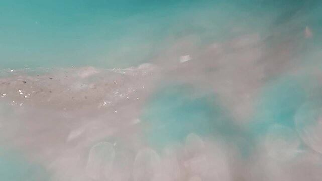 &iacute;deo art&iacute;stico en c&aacute;mara lenta de una ola rompiendo, con espuma blanca y agua turquesa en movimiento vistas en primer plano. La escena tiene un car&aacute;cter abstracto y sensorial, centrado en la textura, 