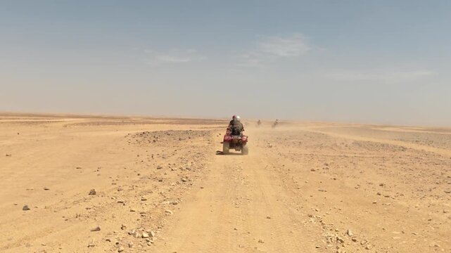 Dynamic point of view footage following a quad bike carrying two riders along a dusty desert trail. Endless arid landscape, rocky terrain and bright blue sky 