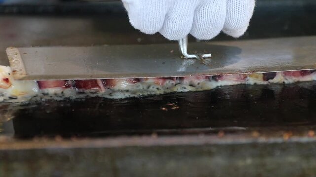Gloved hand flipping squid hot griddle with seafood filling, close up culinary griddle cooking and hand pressing