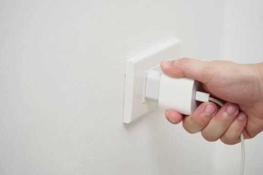 close up hand plugging adapter charge the battery with outlet socket plug and hold mobile phone on wall ,electric safety concept