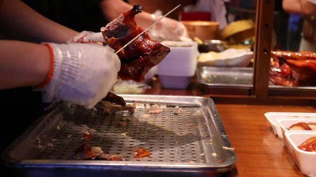 Gloved hands carving roasted poultry and duck perforated metal tray with glossy skin, tender meat, sauce, and food for takeaway busy market counter
