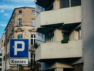 Niebieski znak drogowy końca parkingu na tle miejskiej zabudowy mieszkalnej © Szymon