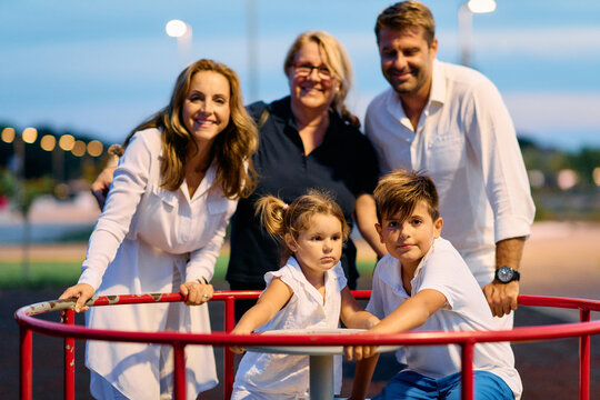 Multigenerational Family Playing on Playground Roundabout at Dusk in Park