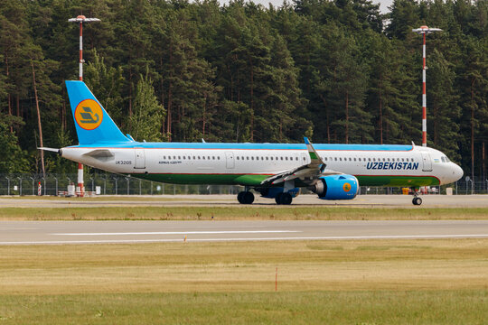 Riga, Latvia - July 06, 2026: Uzbekistan Airways Airbus A321 aircraft taxiing on runway at an airport with green trees and control towers in the background