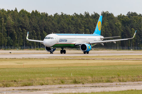 Riga, Latvia - July 06, 2026: Uzbekistan Airways Airbus A321 aircraft taxiing on runway with green grass and trees in the background under clear sky