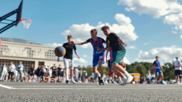 Asphalt basketball court with blurred players in action on a sunny day.