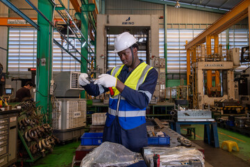Fototapeta premium Worker inspects a part in a factory during the day with machines and coworkers in the background