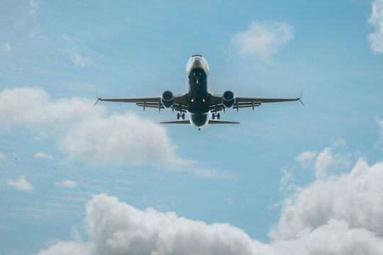Commercial airplane flying overhead against a blue sky with scattered clouds, showcasing the aircraft's underbelly and landing gear in a clear view