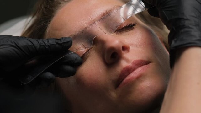 Beautician measuring and preparing a woman's eyebrow for a permanent makeup procedure in a salon
