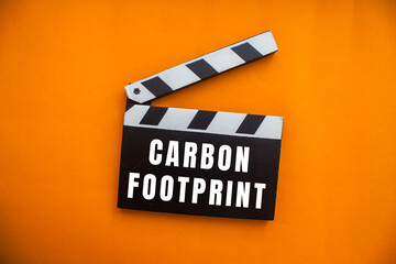 Naklejka premium Clapperboard displaying carbon footprint against an orange background, symbolizing environmental impact and sustainability in cinema