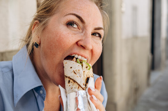 Woman Eating Burrito or Grilled Wrap Sandwich on City Street Enjoying Casual Outdoor Lunch Bite