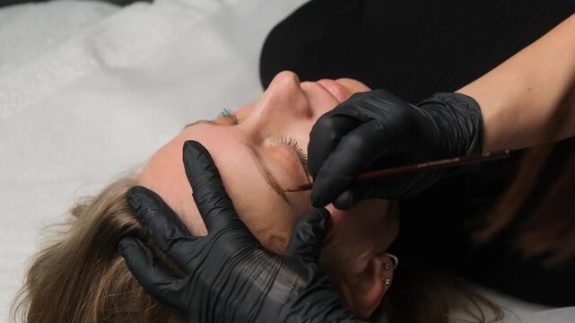 Professional cosmetologist applying permanent makeup to a client's eyebrow in a beauty salon