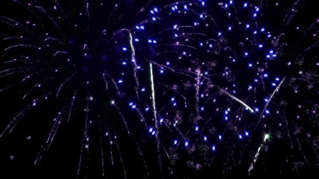 Spectacular blue and purple fireworks exploding in the dark night sky during a festive celebration, holiday event, or New Year's Eve party. 