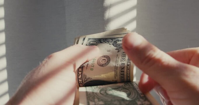 Male hands counting a stack of American one dollar bills in bright sunlight from a window