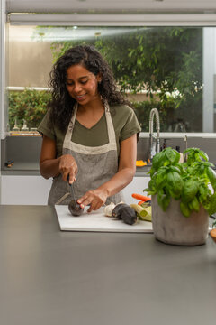 Hispanic woman smiling while cutting avocado in modern kitchen