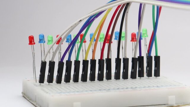 Light emitting diodes of various color glowing in sequence on a breadboard connected with jumper cables. Prototyping patterns of light on an LED