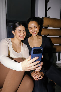 Two young multicultural pleased girlfriends watching mobile phone