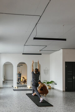 Trainer teach man practice yoga in Parivrtta Ashta Chandrasana pose