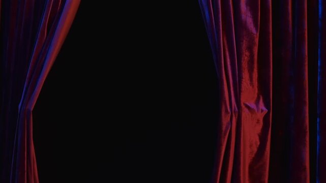Slow motion pan of red velvet curtains parting to reveal dark stage backdrop in theater setting with dramatic lighting and deep shadows